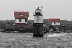 Ram Island Light Between Red Buildings During Storm - BW